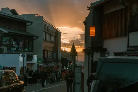 Evening pedestrians passing traditional buildings beneath a glowing sky