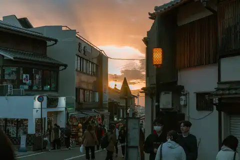 People walking between traditional wooden buildings beneath a warm sunset sky