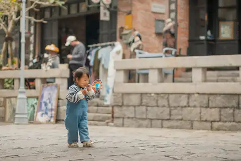 A small child holding a colorful pinwheel in a sunlit courtyard