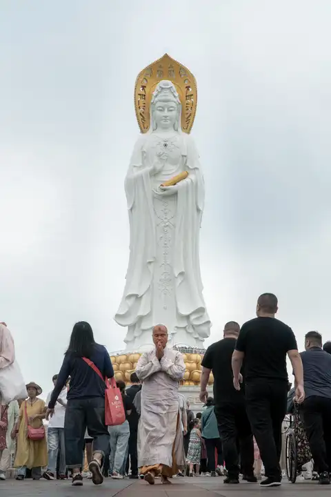 A worshipper walking in prayer beneath a monumental white Guanyin statue