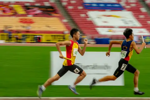 A Hwa Chong relay runner smiling while chasing another runner along the track