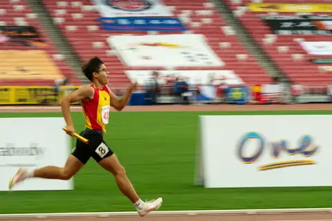 A Hwa Chong relay runner with glasses sprinting while carrying a gold baton