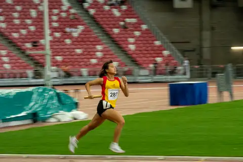 A Hwa Chong relay runner moving across open track with a gold baton