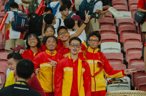 Six Hwa Chong students in red and yellow with painted faces smiling in the stadium stands